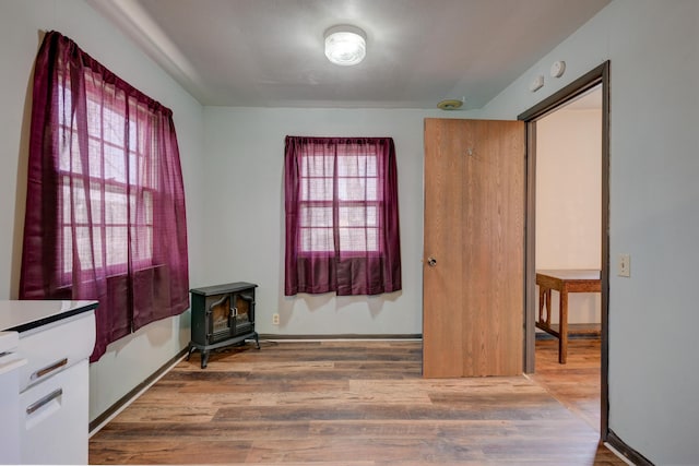 empty room with a wood stove, plenty of natural light, wood finished floors, and baseboards