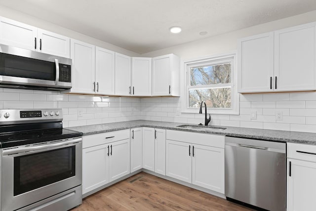 kitchen with light stone counters, a sink, light wood-style floors, appliances with stainless steel finishes, and backsplash