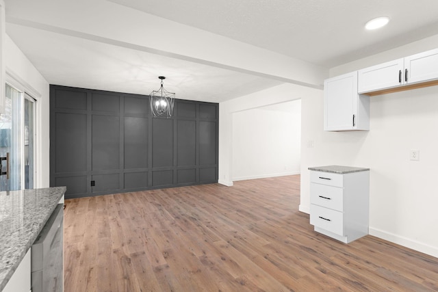 unfurnished dining area with light wood-type flooring, recessed lighting, an inviting chandelier, a decorative wall, and baseboards