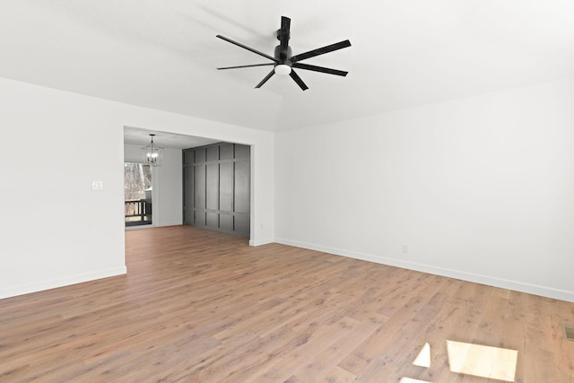 unfurnished room featuring ceiling fan with notable chandelier, light wood-type flooring, and baseboards