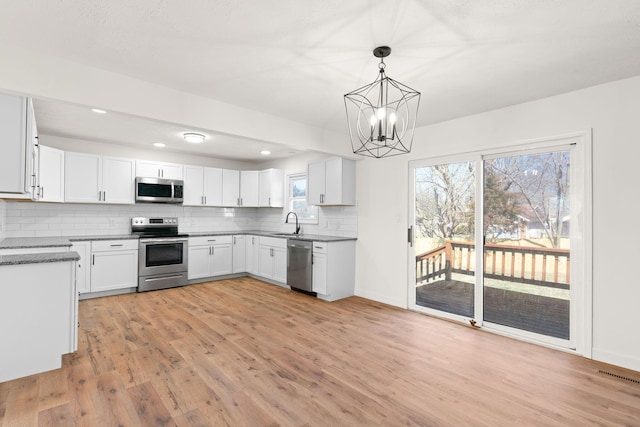 kitchen featuring backsplash, an inviting chandelier, light wood finished floors, and appliances with stainless steel finishes