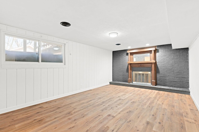 unfurnished living room with a fireplace, brick wall, and wood finished floors