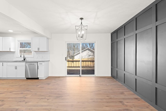 kitchen featuring stainless steel dishwasher, light wood-type flooring, tasteful backsplash, and a sink