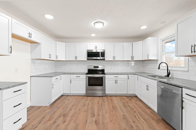 kitchen with light wood finished floors, appliances with stainless steel finishes, light stone countertops, and a sink