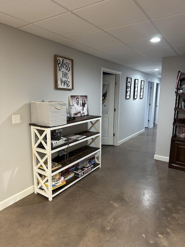 corridor featuring a drop ceiling, baseboards, and concrete flooring