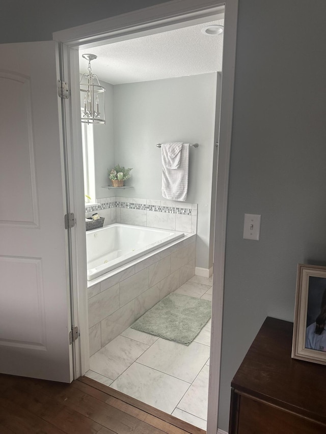 bathroom featuring a bath, wood finished floors, a chandelier, and a textured ceiling