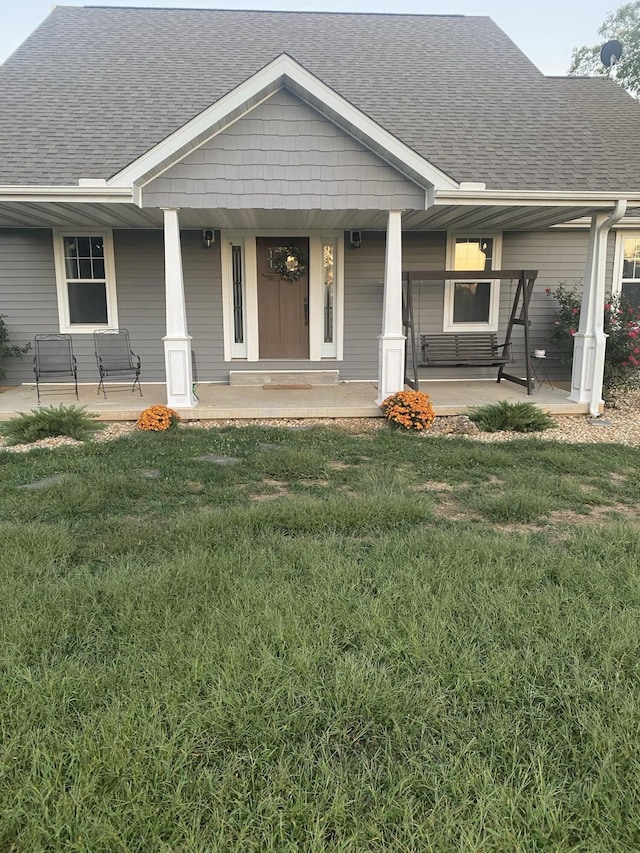 view of front facade featuring a porch, a shingled roof, and a front yard