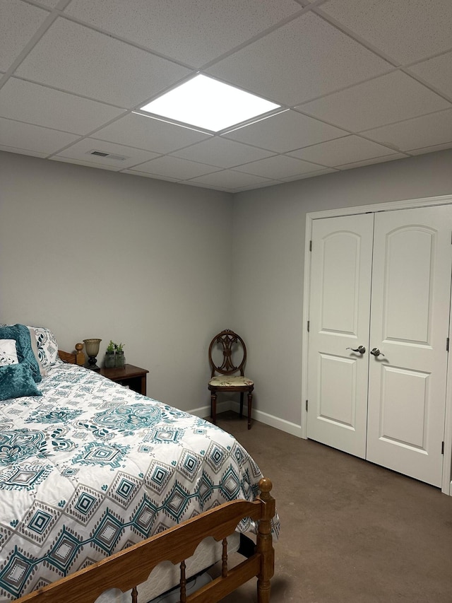 bedroom with a closet, a drop ceiling, dark carpet, and baseboards