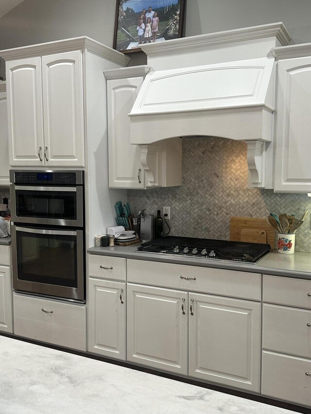 kitchen with backsplash, white cabinetry, stainless steel appliances, and premium range hood