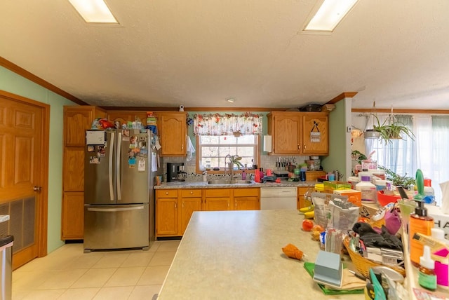 kitchen with light countertops, brown cabinets, freestanding refrigerator, white dishwasher, and a sink