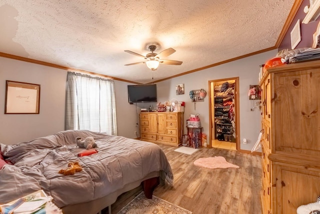 bedroom with a ceiling fan, a textured ceiling, a walk in closet, crown molding, and light wood-type flooring