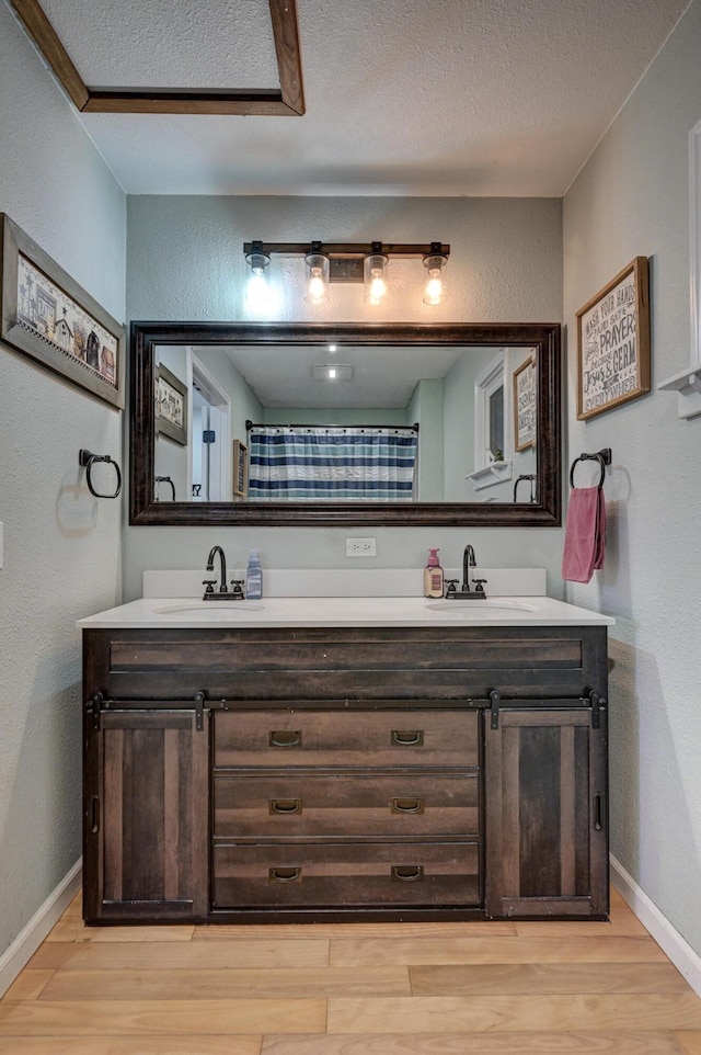 full bath featuring double vanity, wood finished floors, baseboards, and a sink