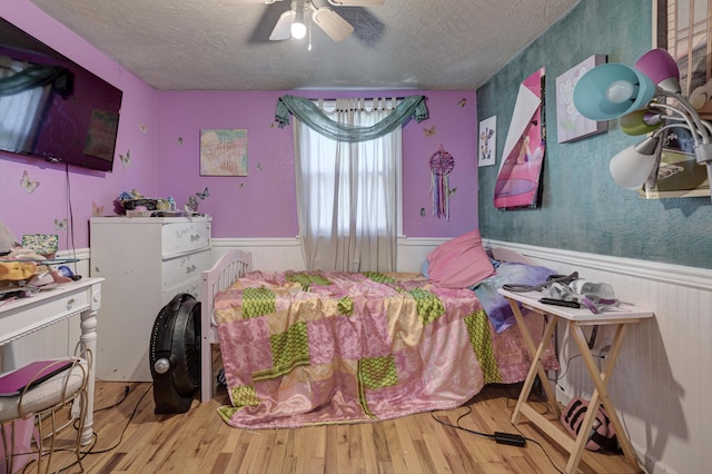 bedroom featuring a textured ceiling, ceiling fan, wood finished floors, and wainscoting