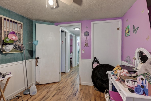 bedroom with ceiling fan, a wainscoted wall, a textured ceiling, and light wood-style flooring