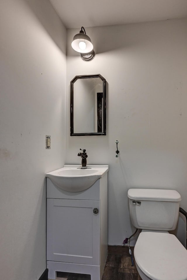 half bath with toilet, vanity, and wood finished floors