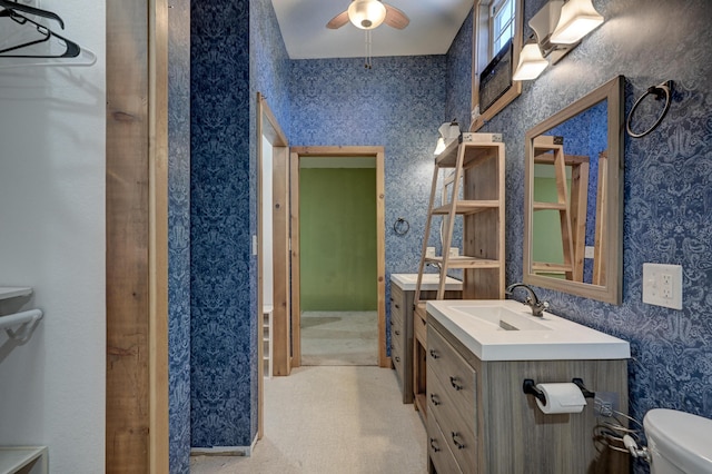 bathroom with a ceiling fan, toilet, vanity, and wallpapered walls