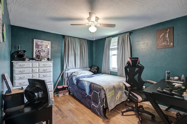 bedroom with light wood finished floors, a textured ceiling, ceiling fan, and a textured wall