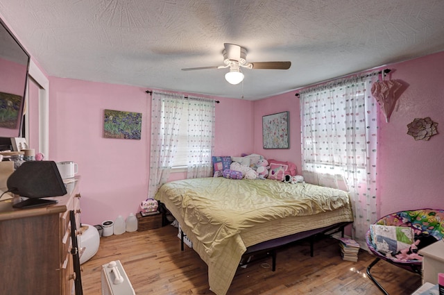 bedroom with multiple windows, a textured ceiling, light wood-style flooring, and a ceiling fan