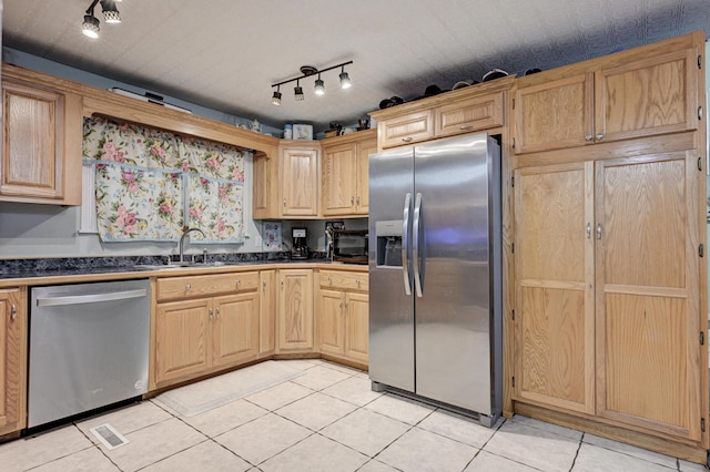 kitchen with dark countertops, light brown cabinetry, light tile patterned floors, appliances with stainless steel finishes, and a sink