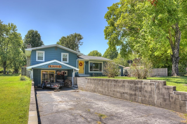 split level home with concrete driveway, fence, a front yard, and a chimney