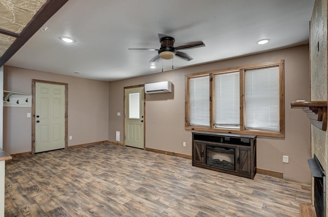 unfurnished living room with a wall mounted air conditioner, baseboards, wood finished floors, and a ceiling fan