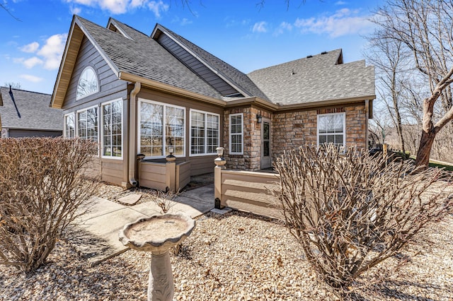 back of property featuring stone siding and roof with shingles