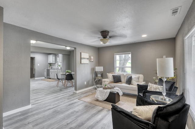 living area with a textured wall, baseboards, visible vents, and light wood finished floors