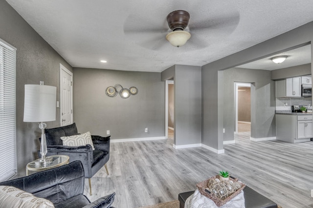 living area featuring ceiling fan, a textured ceiling, baseboards, and light wood-style floors