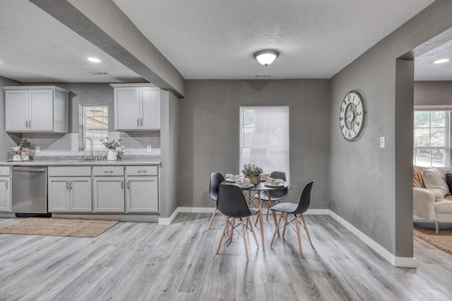 dining area with light wood finished floors, a textured ceiling, baseboards, and a textured wall