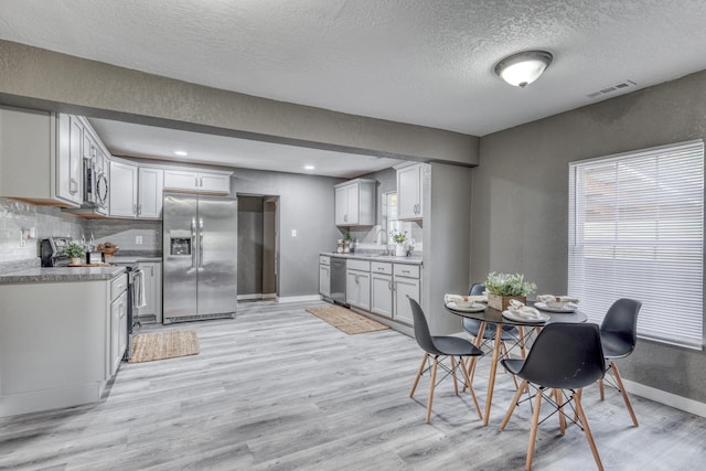 dining room with visible vents, baseboards, light wood-style floors, and a textured ceiling