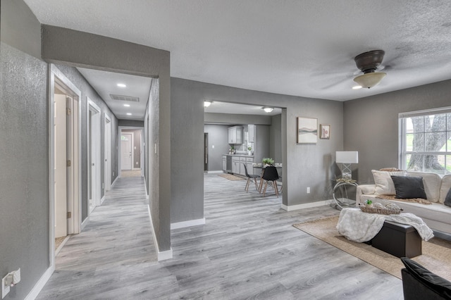 living area featuring light wood finished floors, visible vents, a textured ceiling, and baseboards