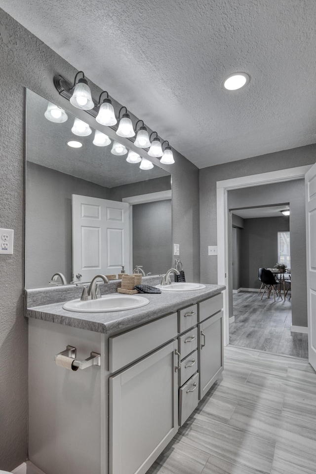 full bath featuring a sink, a textured ceiling, and double vanity