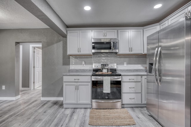 kitchen featuring a textured wall, stainless steel appliances, tasteful backsplash, and light wood finished floors