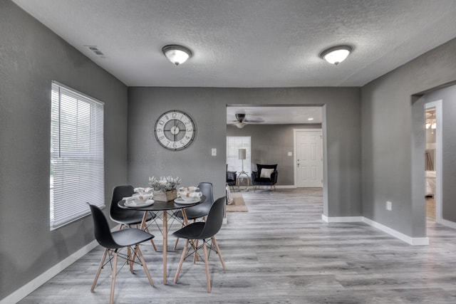 dining room featuring a textured ceiling, wood finished floors, visible vents, and baseboards