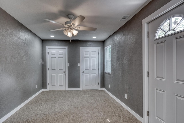 carpeted entryway featuring ceiling fan, a textured wall, visible vents, and baseboards