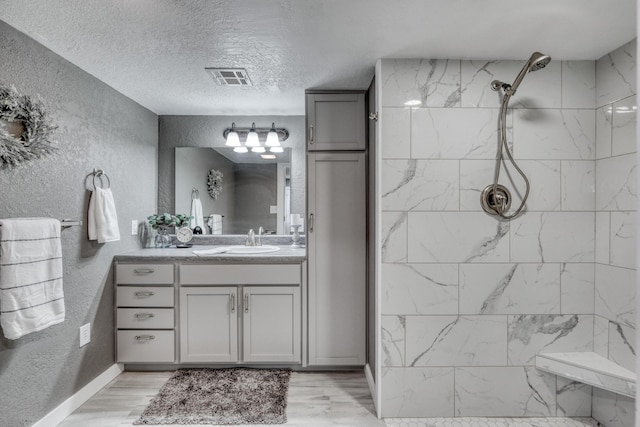 full bathroom with vanity, visible vents, tiled shower, a textured ceiling, and a textured wall