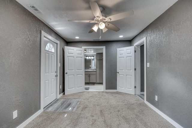 foyer entrance featuring visible vents, a textured wall, light colored carpet, and baseboards