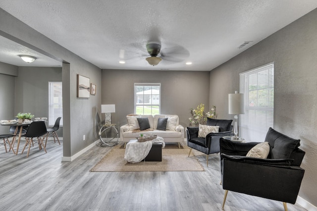 living area with visible vents, ceiling fan, baseboards, wood finished floors, and a textured ceiling