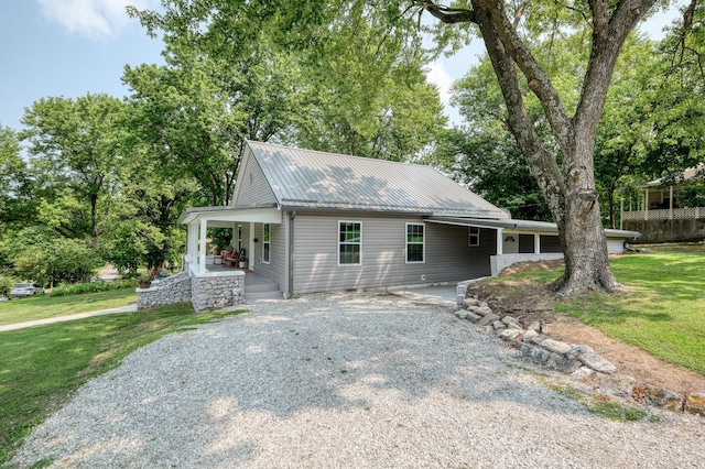 view of front of property featuring gravel driveway, a front yard, covered porch, and metal roof