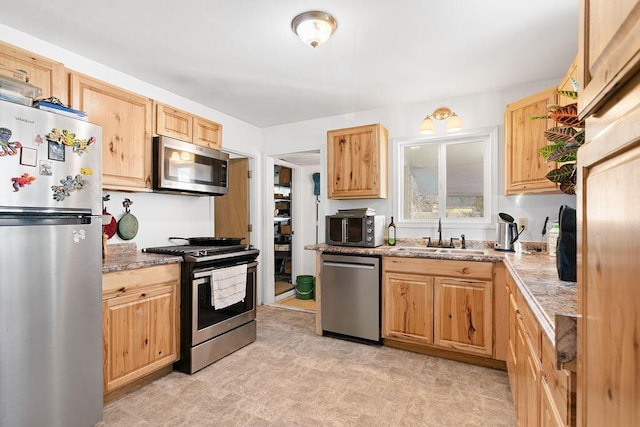 kitchen with light stone counters, appliances with stainless steel finishes, light brown cabinetry, and a sink