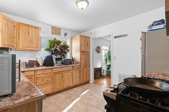 kitchen with visible vents, light floors, light brown cabinets, and freestanding refrigerator