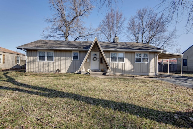 back of property with an attached carport, a chimney, entry steps, aphalt driveway, and a lawn