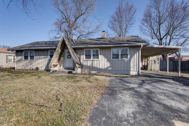 view of front of house with aphalt driveway, fence, a front yard, an attached carport, and a chimney