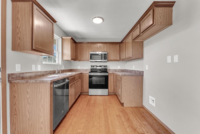 kitchen with a sink, stainless steel appliances, light countertops, and light wood finished floors