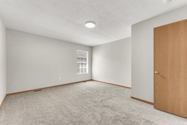 spare room featuring visible vents, a textured ceiling, baseboards, and carpet