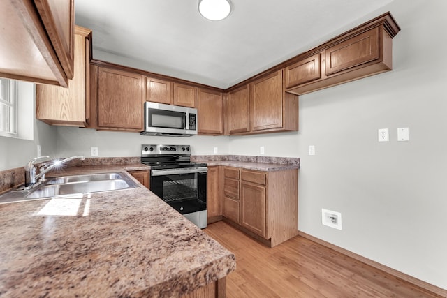 kitchen featuring light wood-type flooring, light countertops, brown cabinets, stainless steel appliances, and a sink