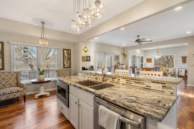 kitchen featuring a kitchen island with sink, a sink, stainless steel appliances, light stone countertops, and dark wood-style flooring