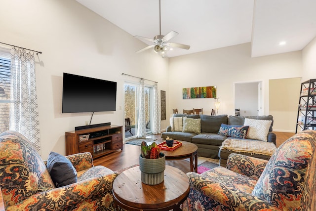 living area featuring ceiling fan, baseboards, wood finished floors, and a towering ceiling