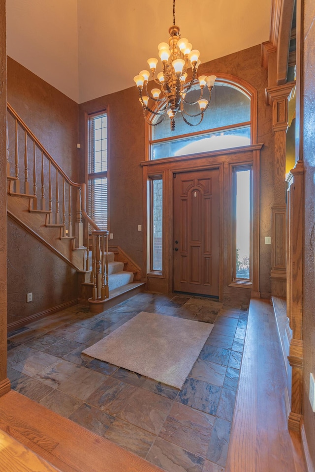 foyer entrance featuring a notable chandelier, stairway, stone finish floor, and a towering ceiling