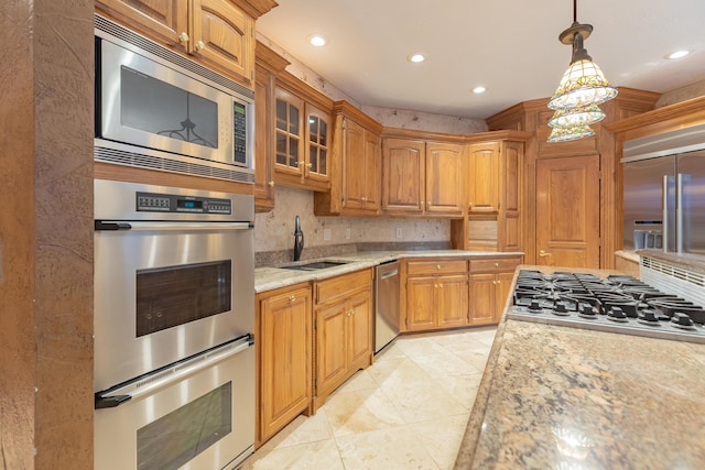 kitchen featuring tasteful backsplash, glass insert cabinets, built in appliances, hanging light fixtures, and a sink